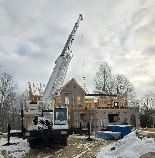 A large white crane is parked in front of a house under construction