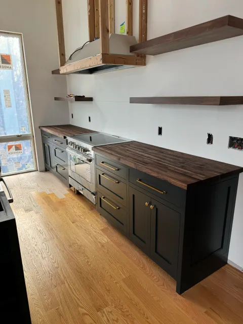Lower custom kitchen cabinets installed next to a stainless steel range with matching floating wood shelves on the wall.