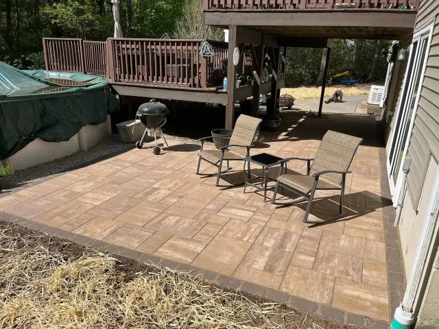 Patio with brown pavers, seating, and a grill, beneath a deck.