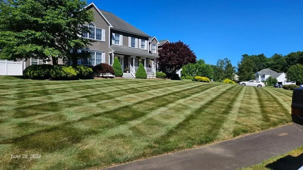 Suburban house with manicured striped lawn on a sunny day, viewed from the sidewalk
