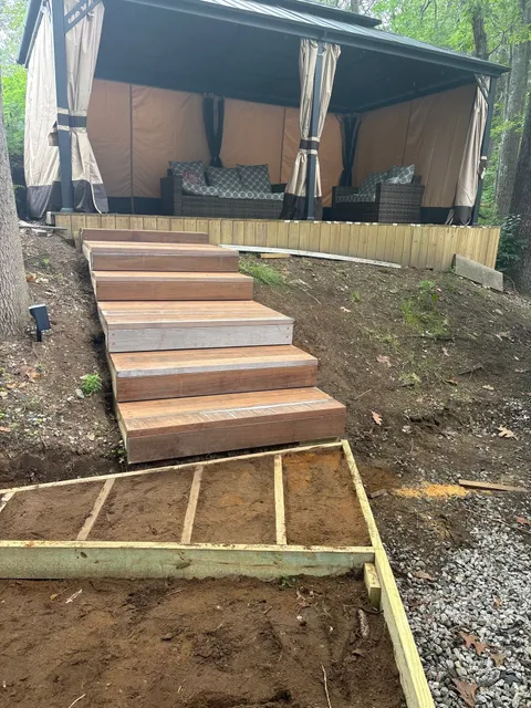 Curved wooden deck stairs leading to a covered outdoor seating area, showcasing a remodeling project for a backyard in Manchester, NH.