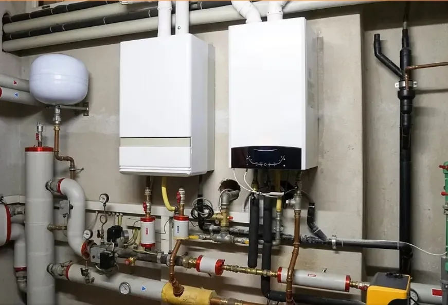 Boiler room with white wall-mounted units, pipes, valves, and a gray expansion tank against a basement wall