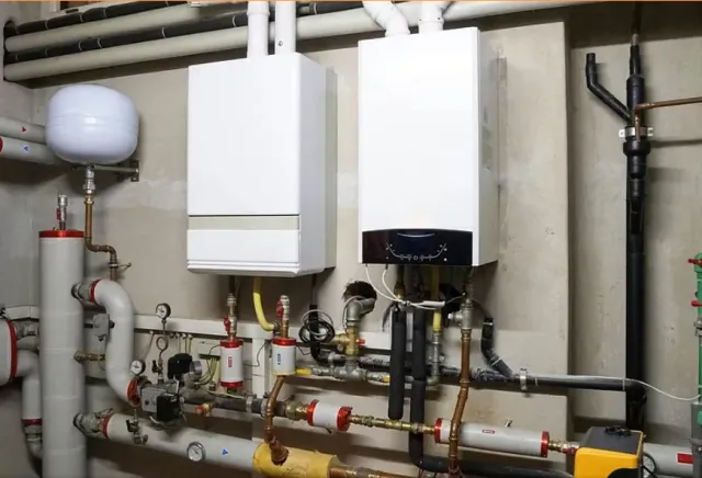 Boiler room with white wall-mounted units, pipes, valves, and a gray expansion tank against a basement wall