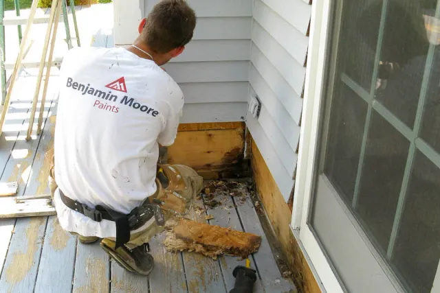 Man hunched over while repairing grey siding on the exterior of a home.