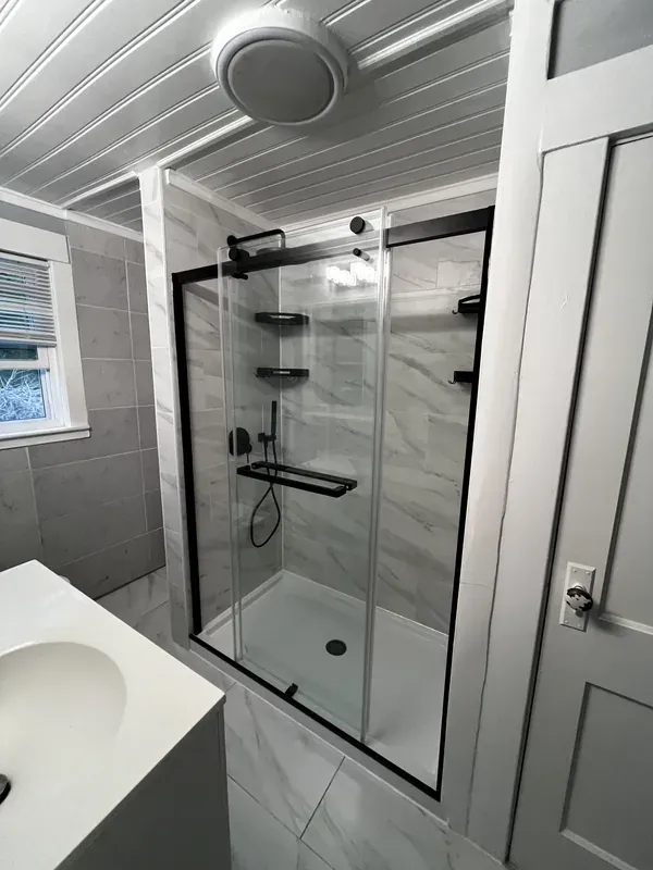 Finished tub-to-shower conversion with sliding glass door and matte black frame