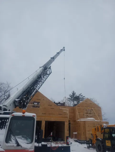 Construction site with crane lifting roof truss onto a house