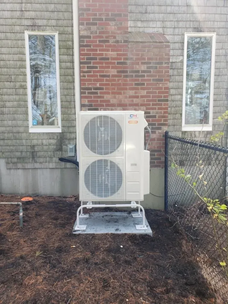 A large air conditioner is sitting in front of a brick building.