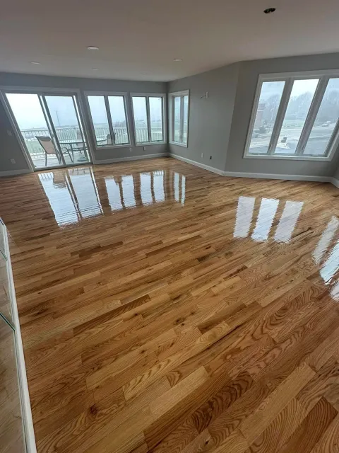 Empty living room with hardwood floors and large windows showing a balcony and outdoor view.