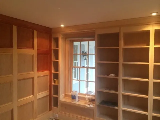 Built-in wooden bookshelves and cabinets in a warmly lit room with a central window.