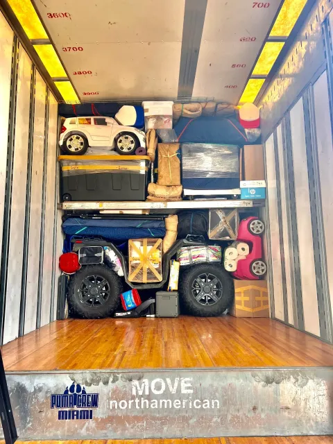 Moving truck packed with furniture, boxes, and a motorcycle, viewed from the open cargo bay.