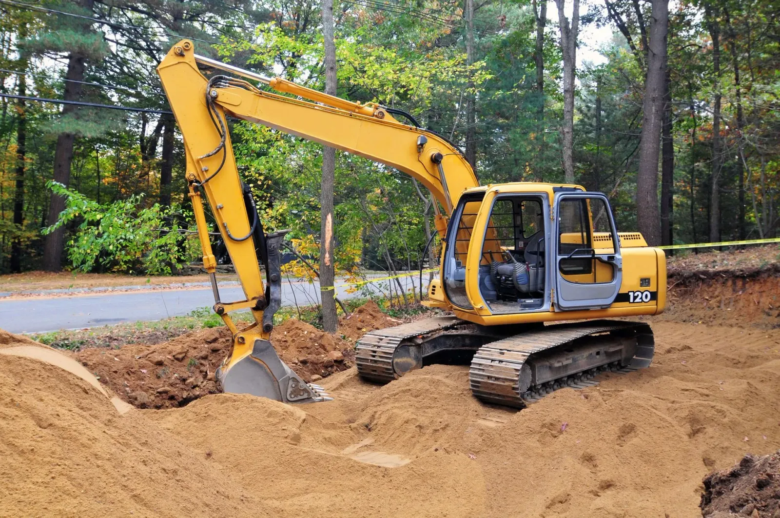 Yellow excavator digging in a dirt pit near trees and a road.