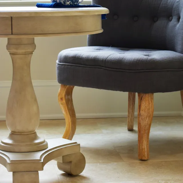 A beige stone tile floor with a light wood pedestal table and a gray upholstered chair.