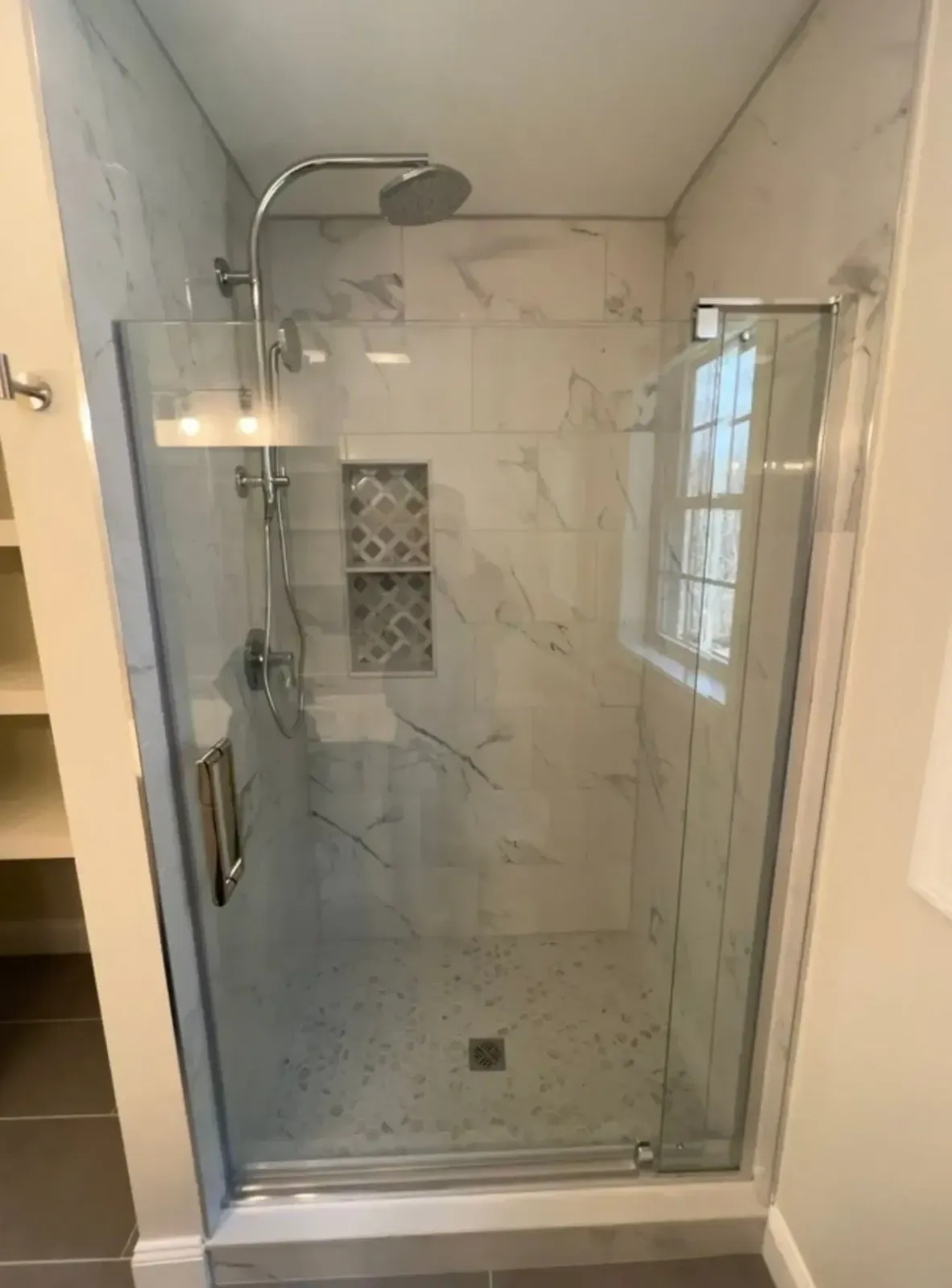 Modern walk-in shower with glass door, marble-look tile, and chrome showerhead.