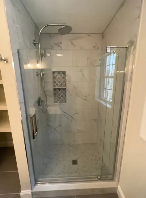 Modern walk-in shower with glass door, marble-look tile, and chrome showerhead.