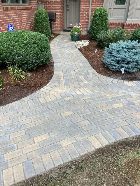 Brick pathway leading to a front door, lined with shrubs and mulch.