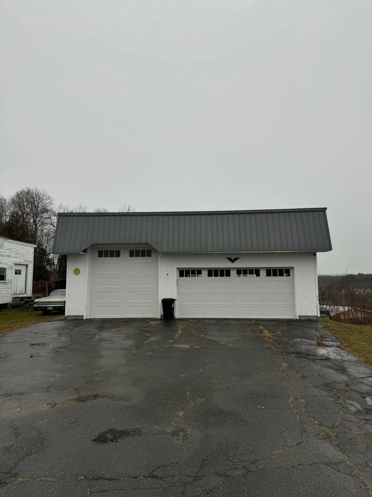 A white garage with a gray roof is sitting on the side of a road.