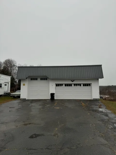 A white garage with a gray roof is sitting on the side of a road.