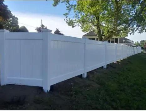 White vinyl privacy fence in a grassy yard, under a blue sky, near a house.