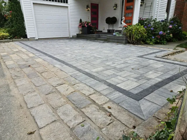 Brick driveway and walkway in front of a white house with a red door.