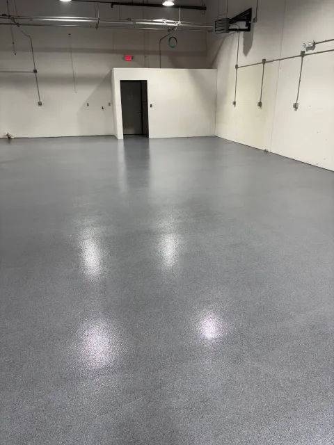 Gray epoxy floor in a large, empty room with white walls and a doorway.