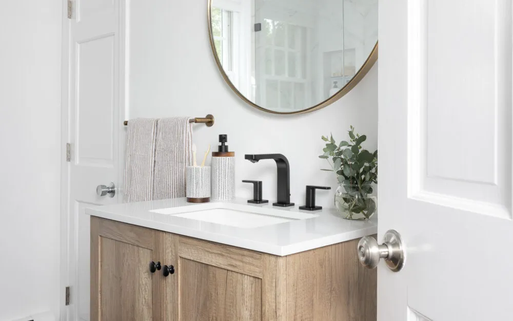 Before photo of bathroom with wood vanity, gold mirror, black floor - Woodland Builders, South Shore MA.