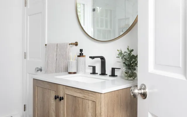 Before photo of bathroom with wood vanity, gold mirror, black floor - Woodland Builders, South Shore MA.