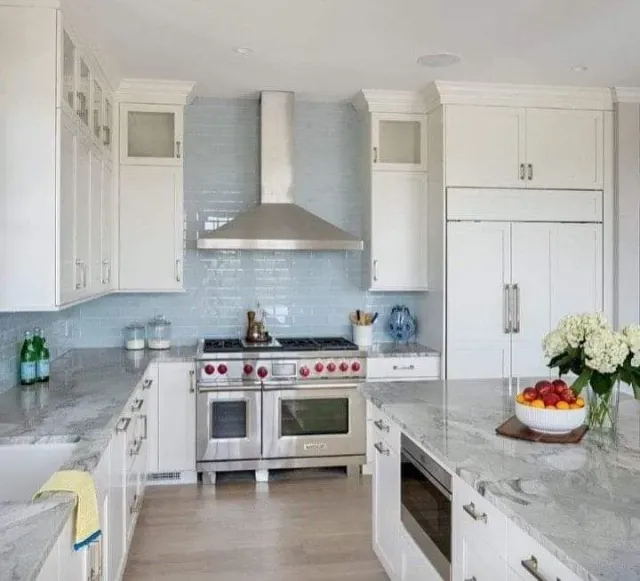 White kitchen with stainless steel appliances, blue backsplash, and marble countertops.