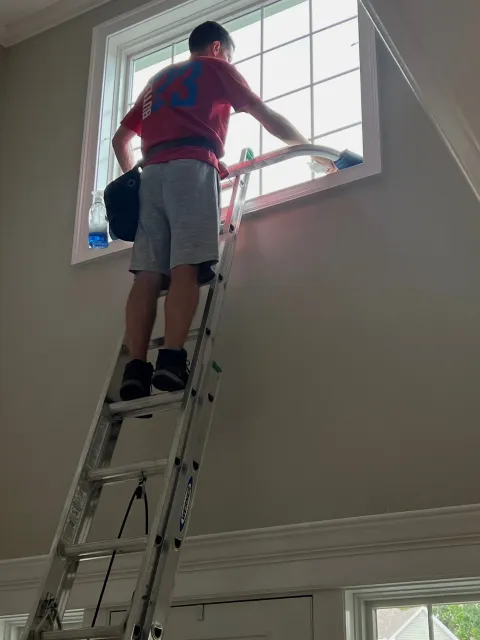 Person cleaning a window while standing on a ladder indoors.