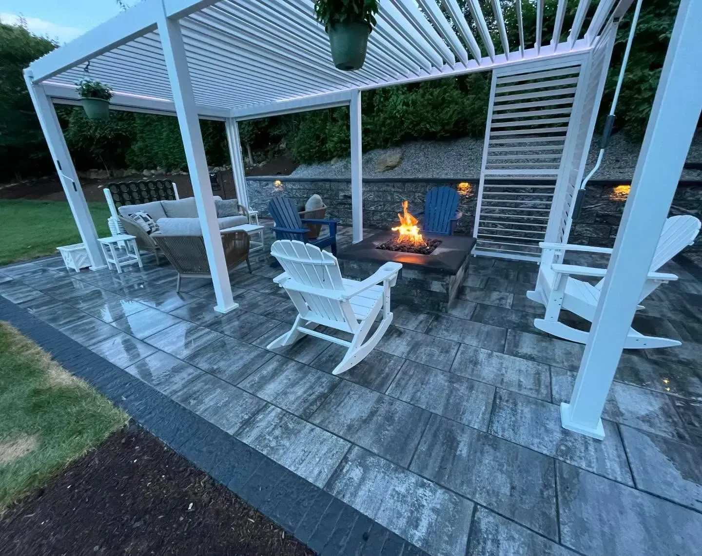 Patio with fire pit, pergola, Adirondack chairs, and seating. Fire is lit.