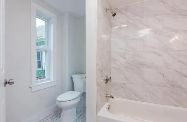 A bathroom with a toilet, tub, shower and window.