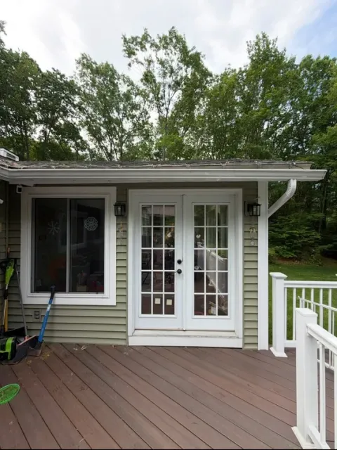 White French doors on a small house deck with railing and trees in the background