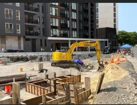 Construction site with a yellow Komatsu excavator, building foundations, and construction materials in an urban area.