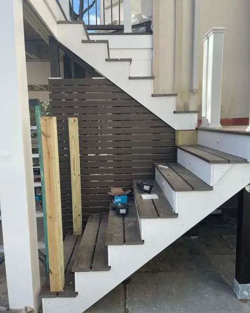 Staircase under construction with dark wood steps and brown slatted wall. Two wooden posts stand nearby.