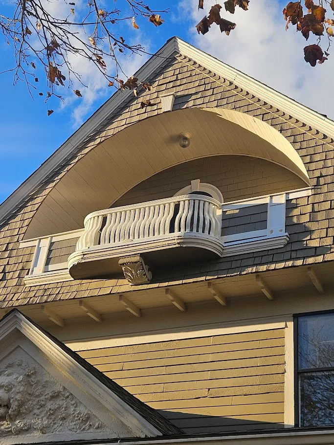 Restored curved third-story porch with a white balustrade under an arched gable on a historic shingle home in Cranston, Rhode Island by Toensing Construction