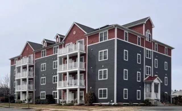 Multi-story apartment building with red and dark gray exterior, white balconies, and multiple windows.