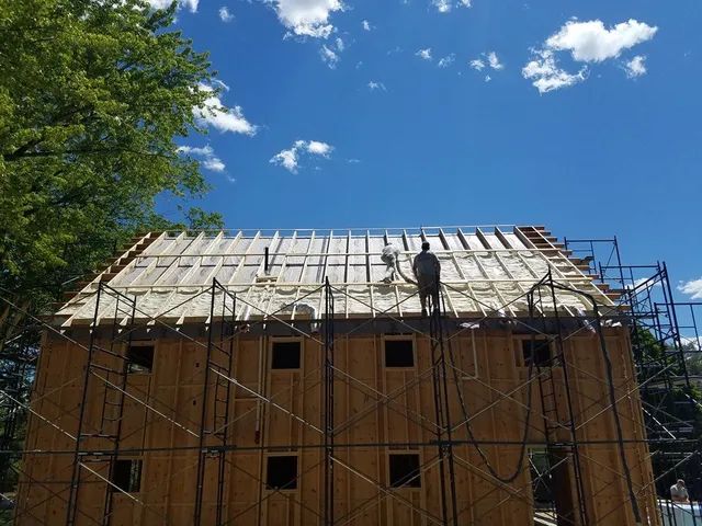 Maine-ly Foam crew spraying foam insulation across an open roof deck on a two-story home in Denmark, Maine
