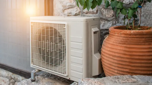 A white air conditioner is sitting on the side of a building next to a potted plant.