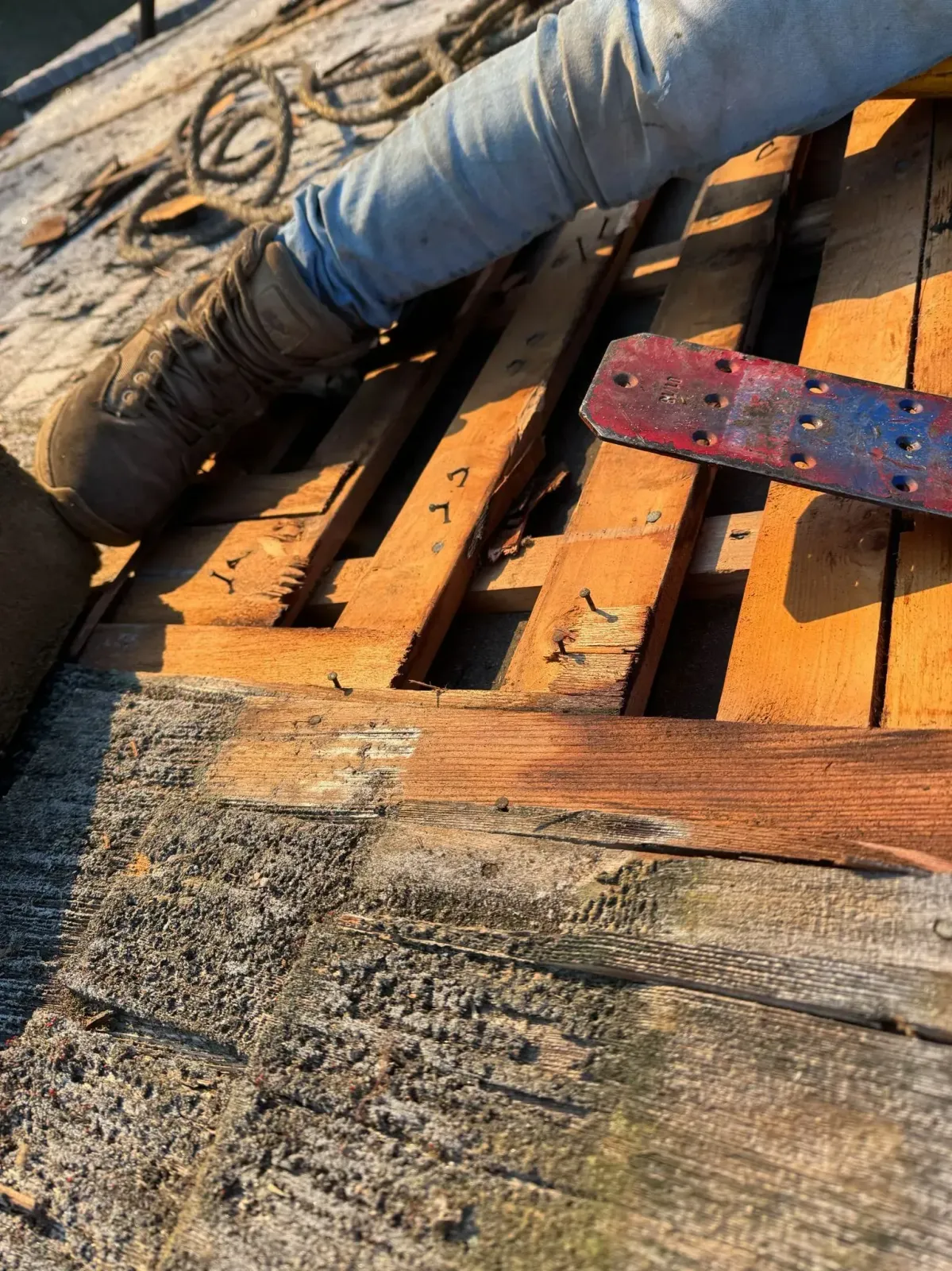 Rusted wood planks, and gray gravel. A blue and red tool, and a gray hose are present on the wood.