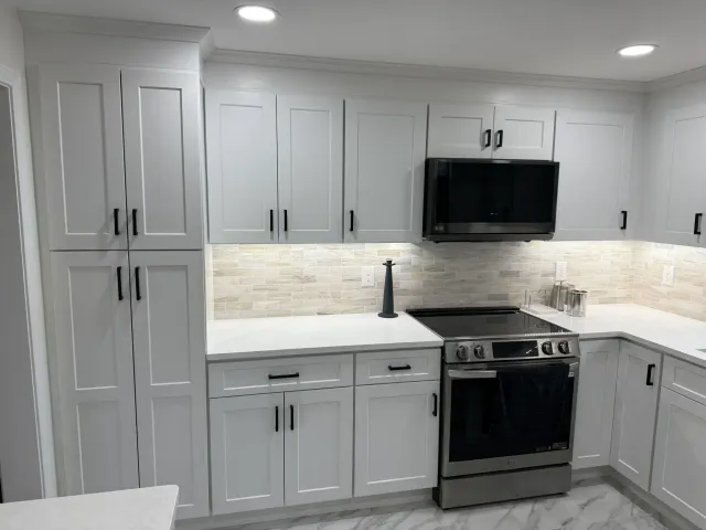 Close-up of white shaker cabinets with black hardware and a natural stone tile backsplash in a Framingham kitchen.