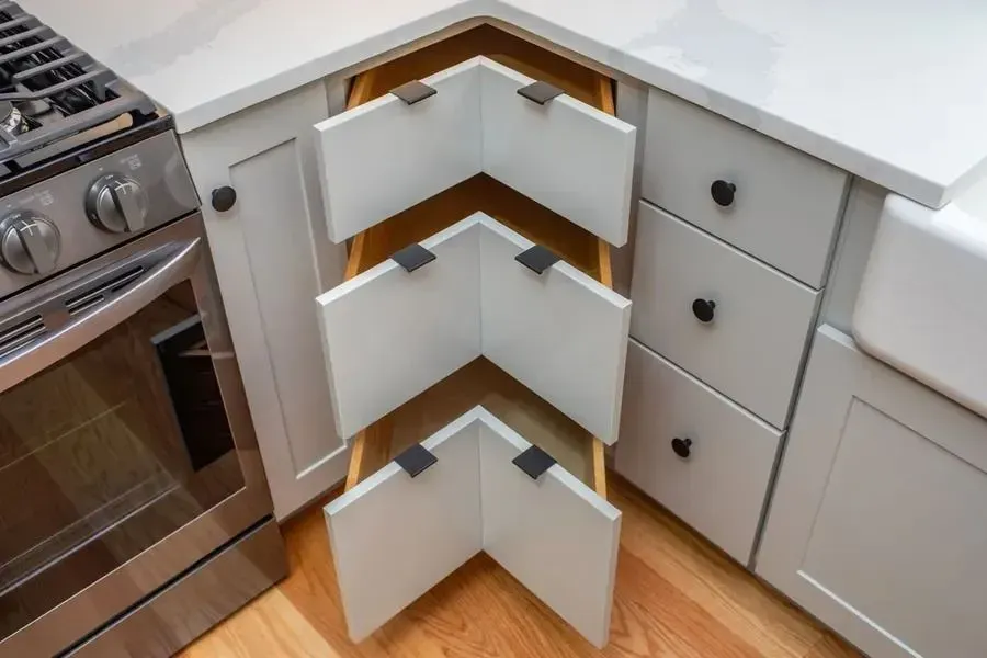 Open corner kitchen cabinet with white shelves and gray drawers beside a stove and countertop