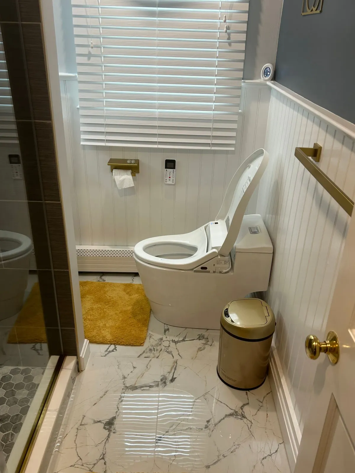 A modern bathroom with a white toilet, gold accents, and a marble floor.