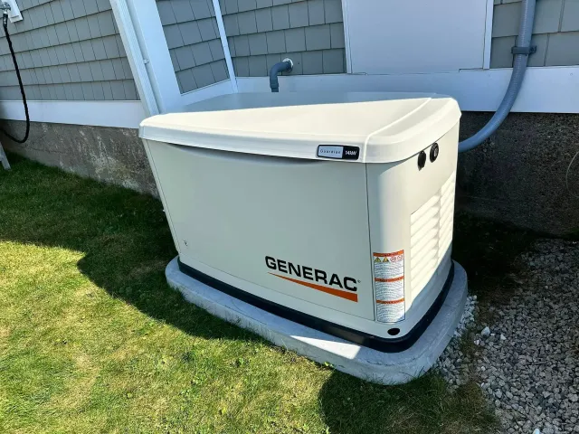A generator is sitting in the grass next to a house.