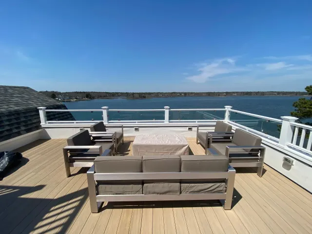 Outdoor deck with modern furniture, water view, and clear blue sky.
