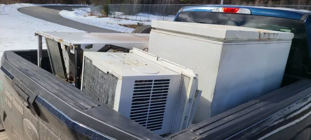 White HVAC unit and metal equipment strapped in pickup truck bed on a snowy road