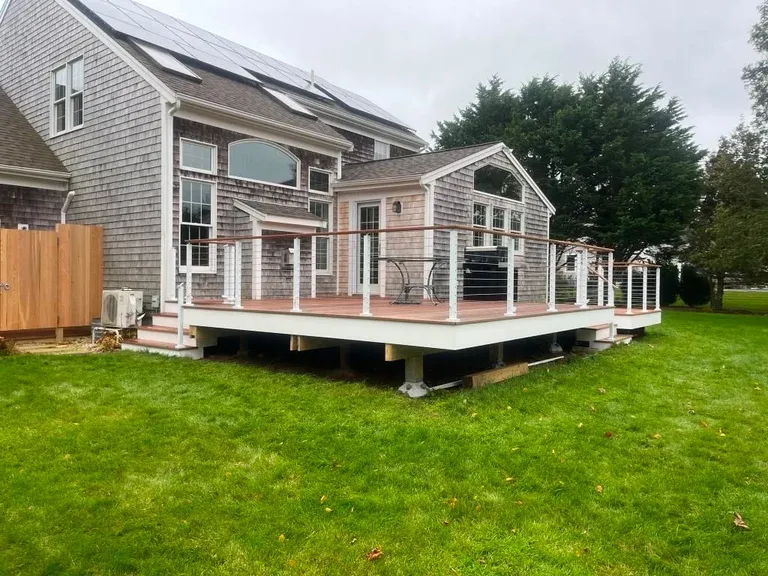 Modern cottage-style house with wooden deck and large windows set on manicured lawn