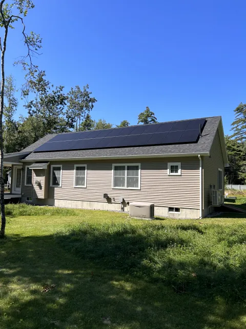 House with solar panels on roof and grassy yard.