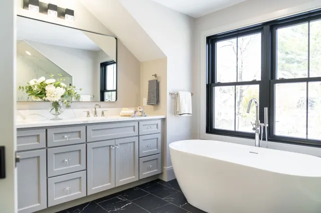 Modern bathroom with gray vanity, large mirror, black-framed windows, and a freestanding white tub