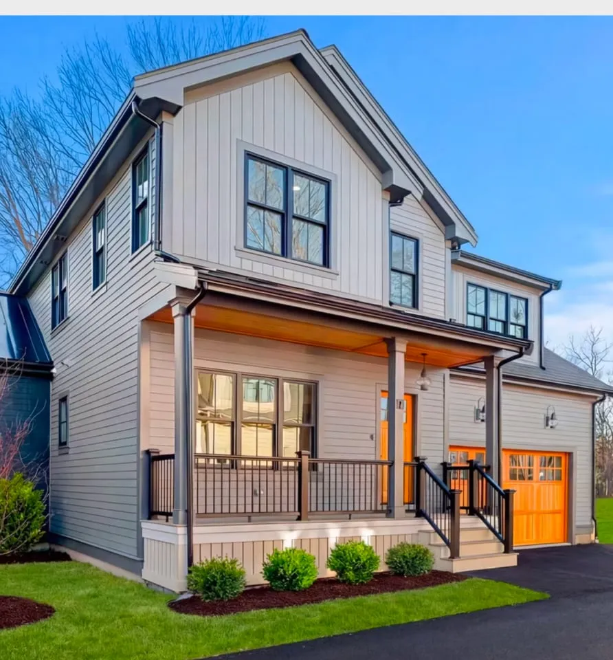 Two-story modern house at 17 Smith Place with gray siding, black trim, a covered front porch, and an orange front door and garage door, plus a driveway and trimmed bushes in front.