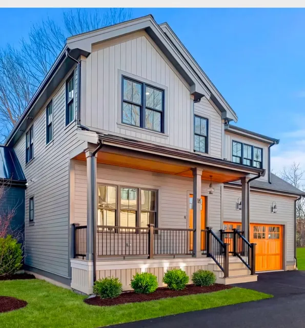 Two-story modern house at 17 Smith Place with gray siding, black trim, a covered front porch, and an orange front door and garage door, plus a driveway and trimmed bushes in front.