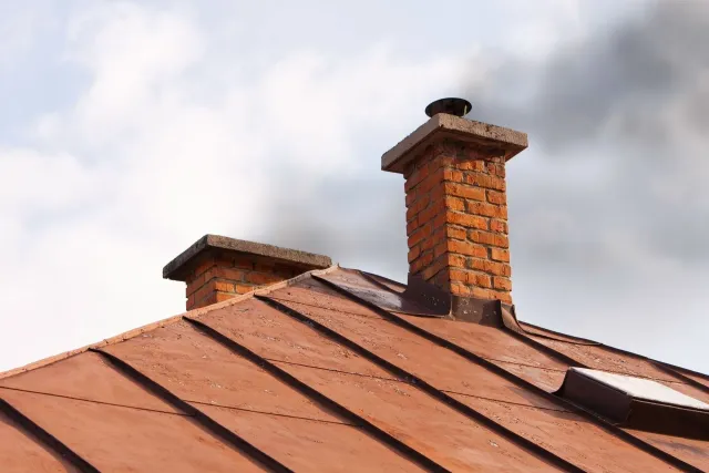 Brick chimneys on a copper-colored roof against a cloudy sky.